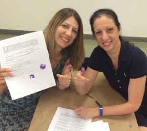 Sue Walia (left) and Rosemarie Hartnett execute Sue’s contract renewal with a purple thumbprint.